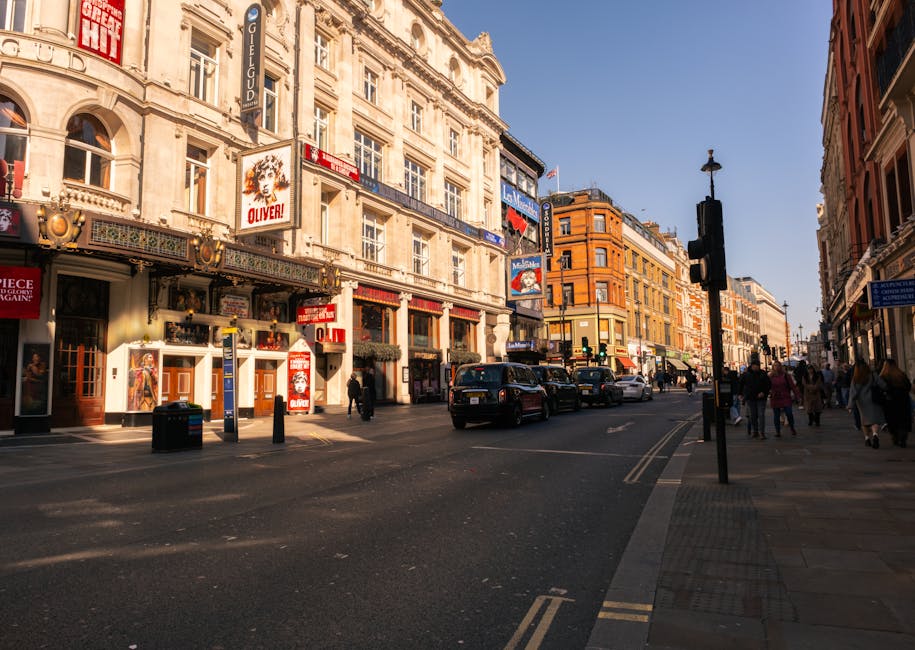 A busy urban street scene depicted in the late afternoon or early evening, with historic multi-story buildings lining both sides. The buildings have ornate architectural details, large windows, and de